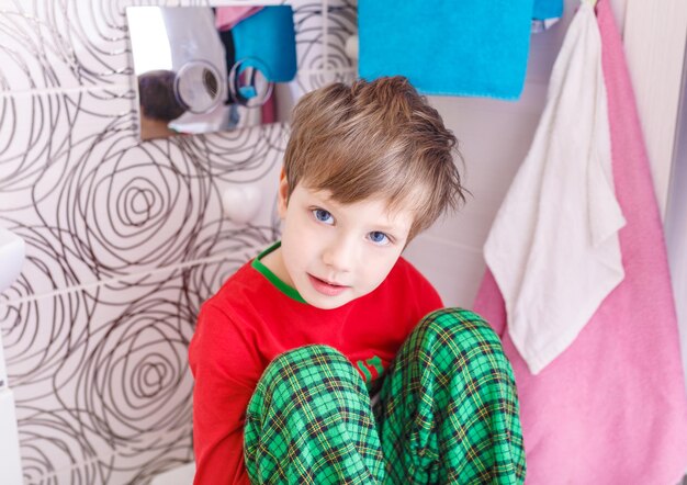 Funny kid sitting in the bathroom on top of the toilet