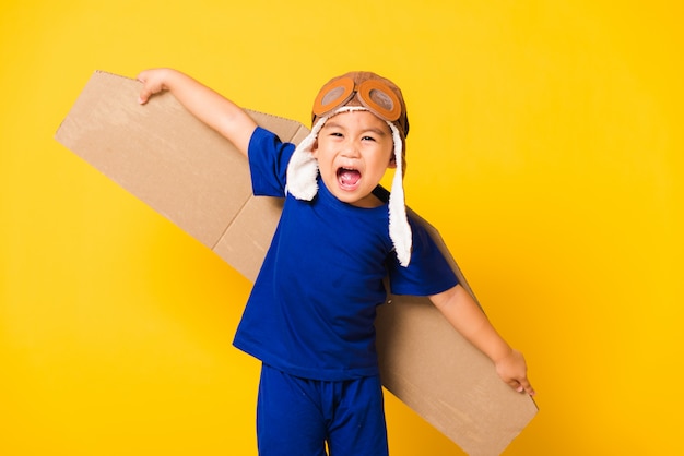 Funny kid smile wear pilot hat playing and goggles with toy cardboard airplane wings flying