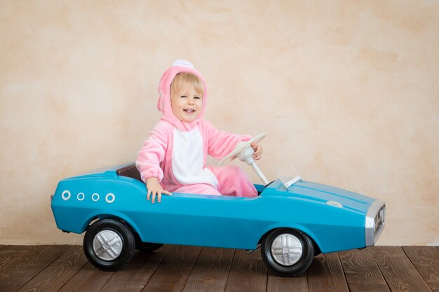 Funny kid wearing Easter bunny. Child riding toy car at home.