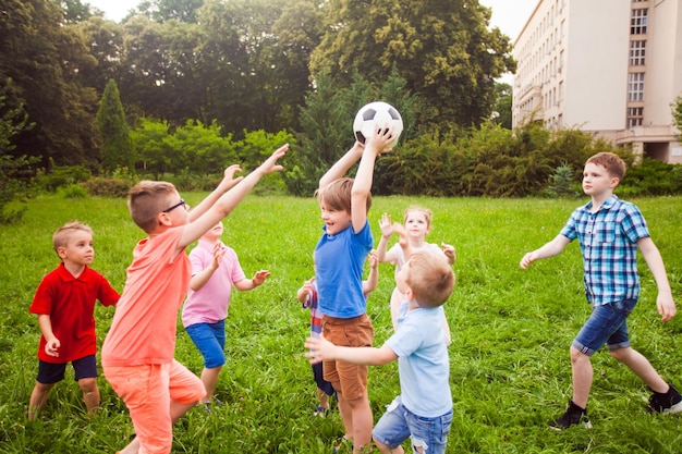 The funny kids are trying to pick up the ball from each other Little boys and girls are actively resting outdoors