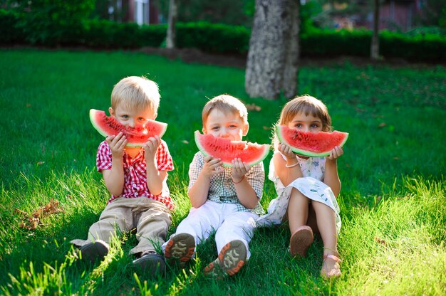 Funny kids eating watermelon outdoors in summer park.