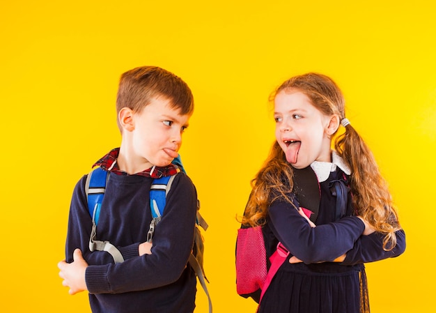 Funny kids in school uniform having fun together Kids showing tongue each other School children isolated over yellow background School friends friendship and relationship