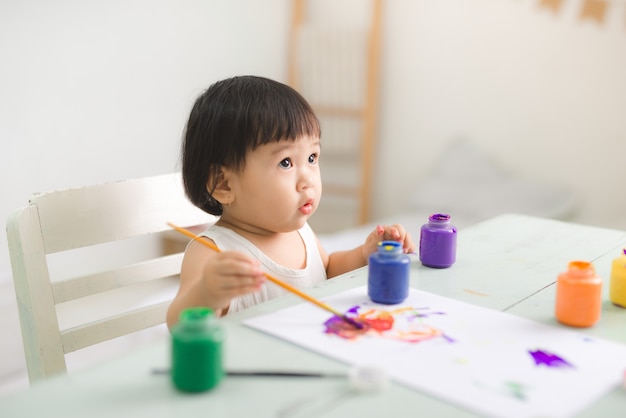 Funny laughing asian baby girl drawing with colorful pencils at home