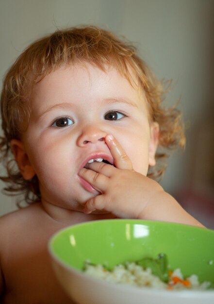 Foto piccolo bambino divertente in cucina che mangia con le dita dal piatto