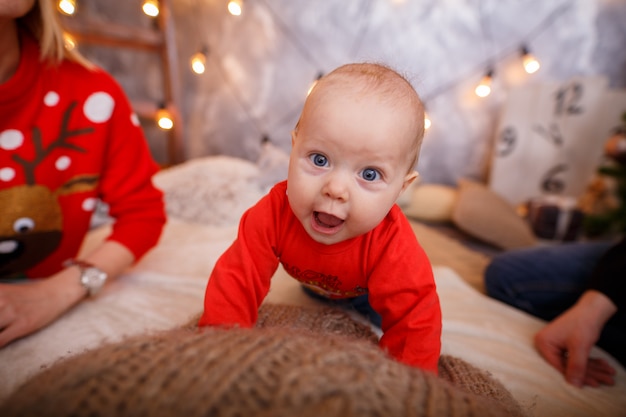 Photo funny little baby in a red sweater. new year's baby photo. the child learns to crawl