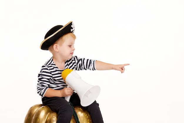Photo funny little boy in carnival costumes of pirates standing with a big pumpkin on white