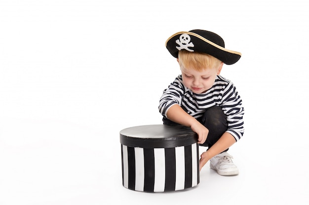 Funny little boy in carnival costumes of pirates standing with a big pumpkin on white