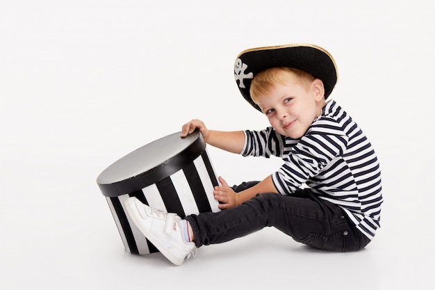 Funny little boy in carnival costumes of pirates standing with a big pumpkin on white