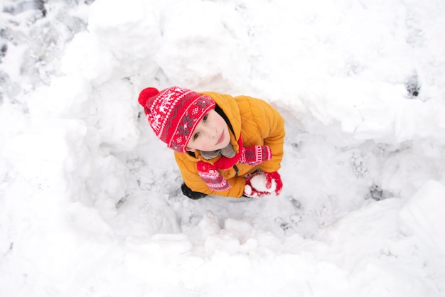 Funny little boy in colorful clothes playing outdoors during a snowfall