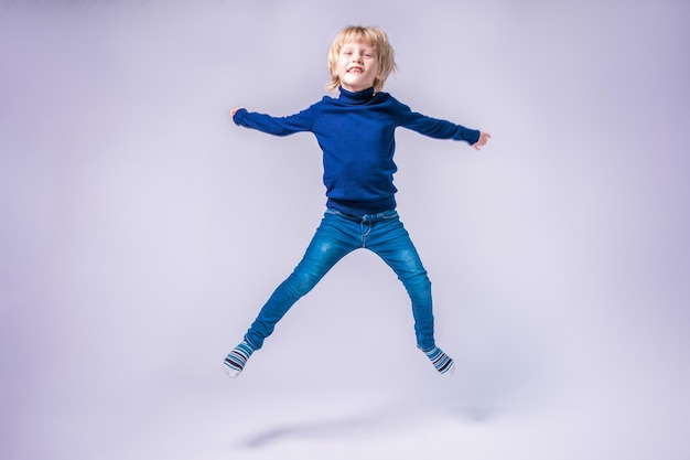 Funny little boy jumping Hands and feet apart In a studio