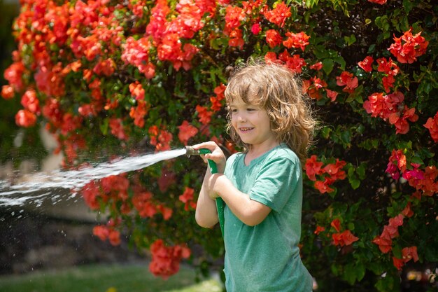 Funny little boy playing with garden hose in backyard child having fun with spray of water summer ou