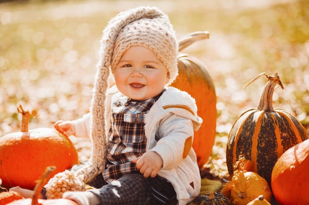 Funny little child sits among pumpkins on the fallen leaves 