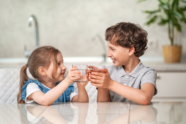 Funny little children drink water in the kitchen at home