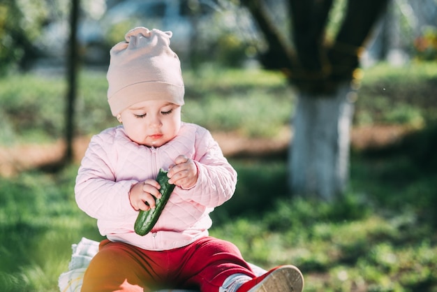 Funny little girl eating fresh cucumber in the garden in spring