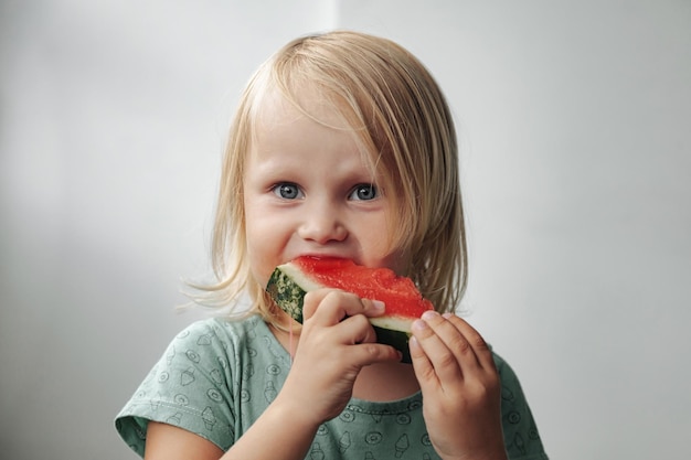 Funny little girl eating watermelon closeup Cute child with watermelon indoors Concept of healthy food summertime Copy space