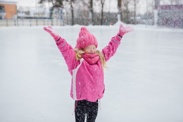 Funny little girl having fun in beautiful winter park during snowfall.