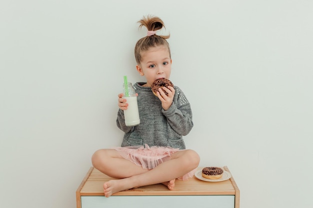 Funny little girl is sitting on the commode with chocolate donut and bottle of milk