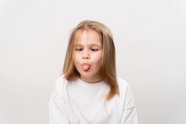 La bambina divertente mostra la lingua e le smorfie su bianco.