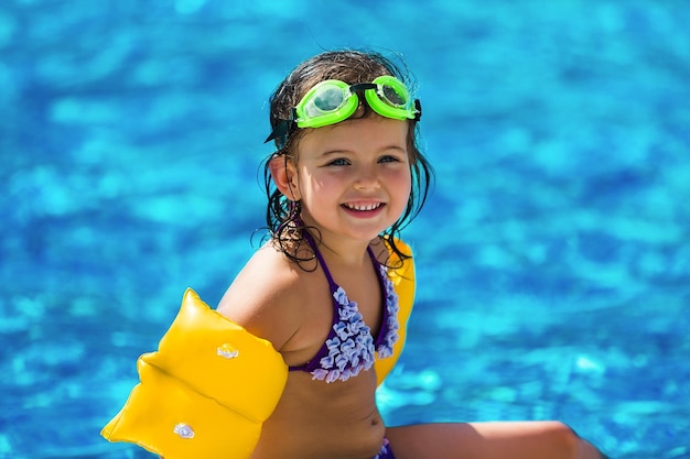 Funny little girl swims in a pool in yellow inflatable armbands