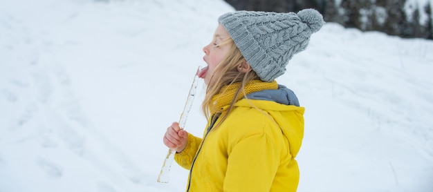 冬の日に雪を食べて歩いている面白い女の子。興奮したクリスマス休暇。子供の風邪やインフルエンザの概念。雪で舌、つららをなめる子供。