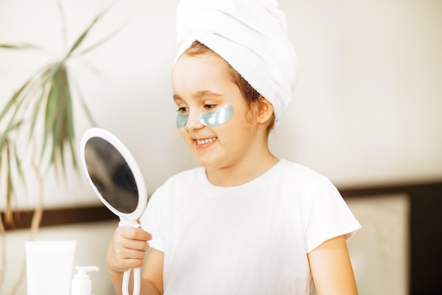 Funny little girl with towel on her head with eye mask looking in a mirror