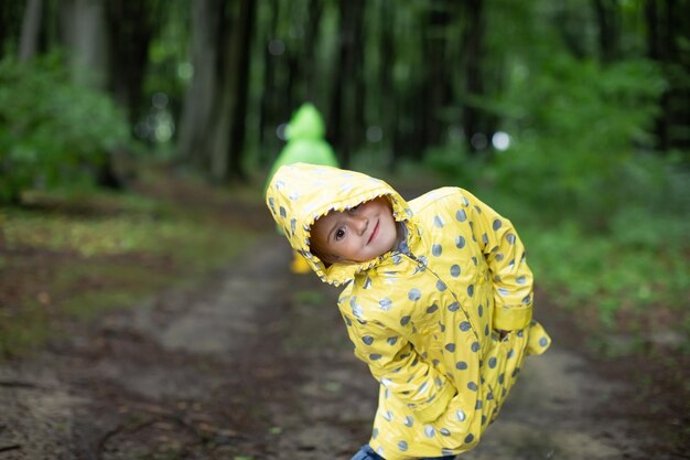 Забавная маленькая девочка в желтом плаще улыбается в весеннем лесу