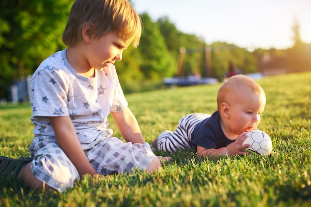 Bambini divertenti che giocano con la palla su erba verde sulla natura al giorno di estate. due fratelli all'aperto. ragazzo e bambino in età prescolare. bambini che giocano in giardino.