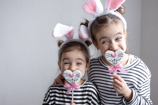 Funny little sisters with Easter gingerbreads in the form of bunny faces and with bunny ears.