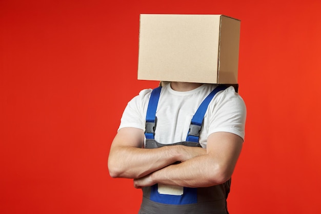 Funny loader with a box on his head stands confidently on a red background