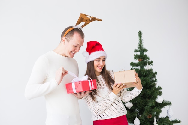 Funny loving couple near Christmas tree. Man wears deer horns and woman wears santa hat.