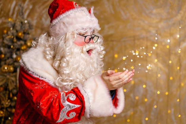 Funny man dressed as santa claus with big white beard on decorated background with bright glowing ga...