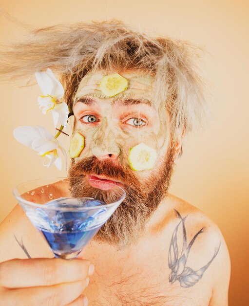 Funny man in hawaii male model with clay mask and cucumber\
slices on face drink cocktail man having