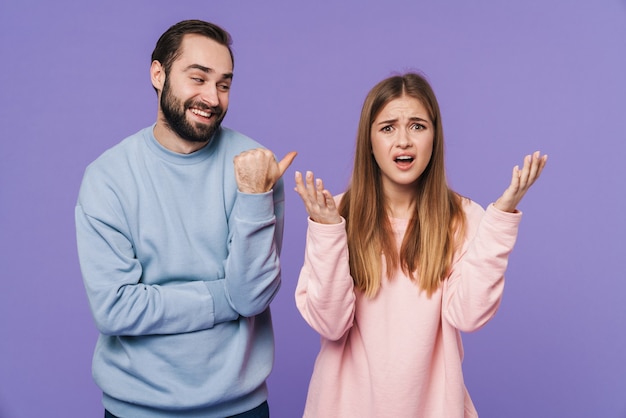 funny man laughing of confused girlfriend isolated over purple wall.