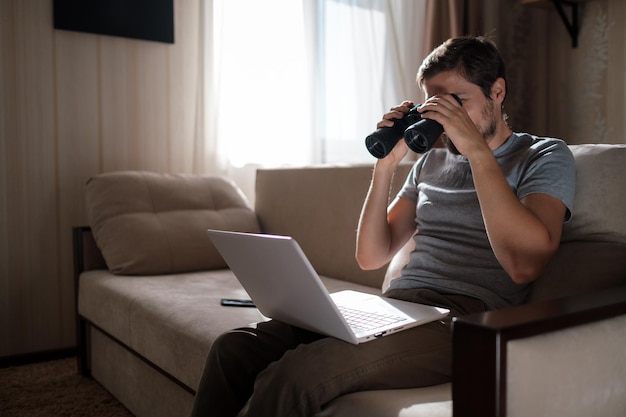 Funny man looking searching binoculars a laptop on the table working at home office