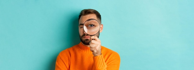 Foto uomo divertente che guarda attraverso la lente d'ingrandimento cercando o indagando su qualcosa in piedi in arancione