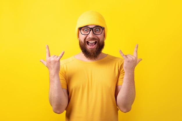 Funny man makes rock n roll gesture over yellow background