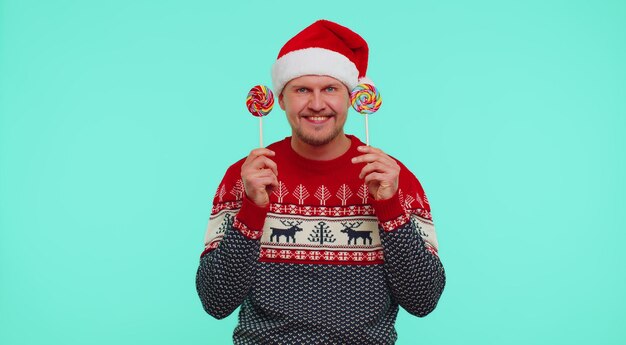 Funny man in red new year sweater holding candy striped lollipops hiding behind them fooling around