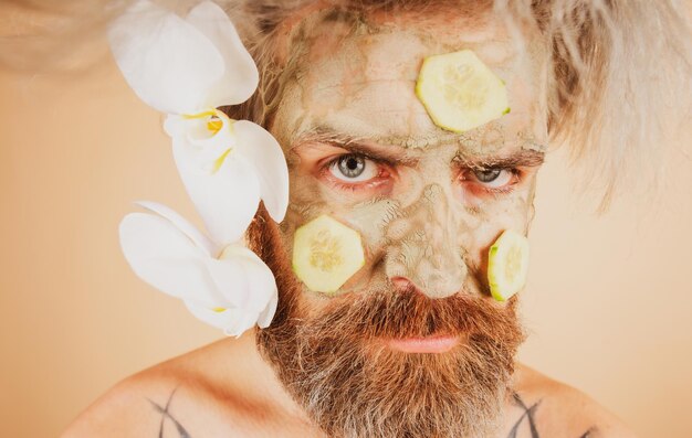 Funny man with clay mask and cucumber slices on face male spa dermatology wellness and facial treatm