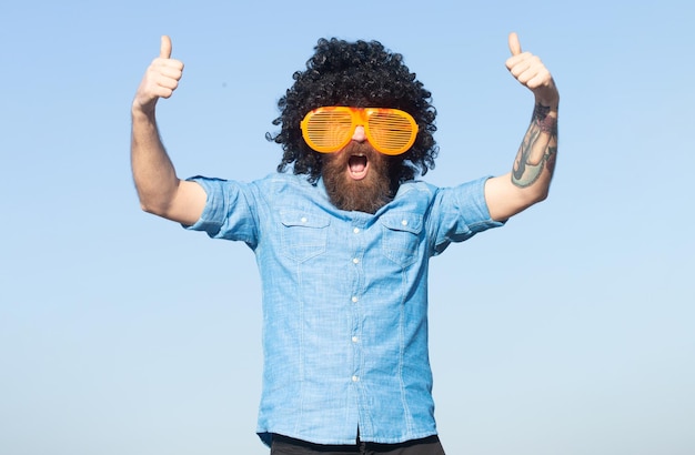 Funny man with large glasses Crazy funny bearded man with wig and fun glasses on sky background