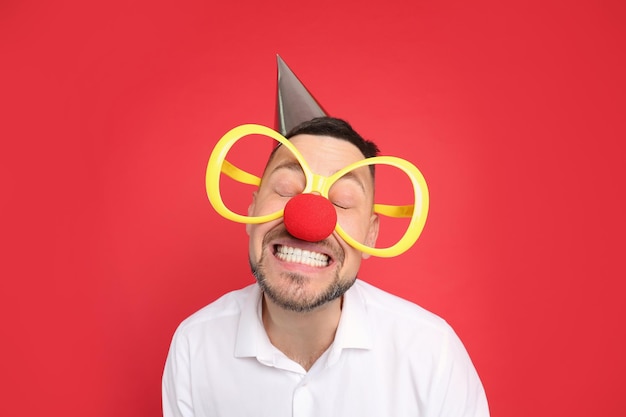 Funny man with large glasses party hat and clown nose on red background April fool39s day