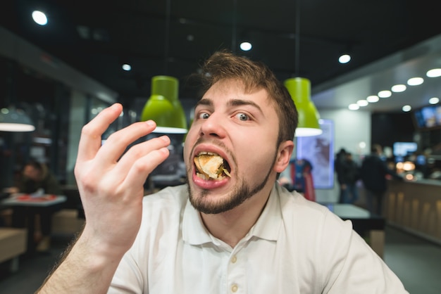 食べ物でいっぱいの口を持つ面白い男。空腹の男はファーストフードの完全な口を手に入れました