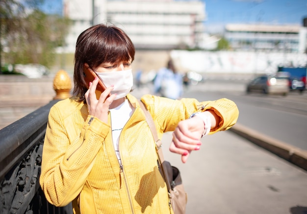 Funny middle-aged woman in a white protective mask talking on a smartphone