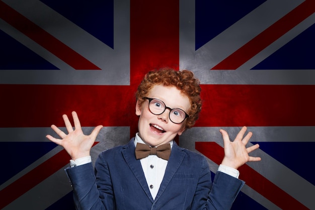 Funny mischievous child boy student against the UK flag background Learn English concept