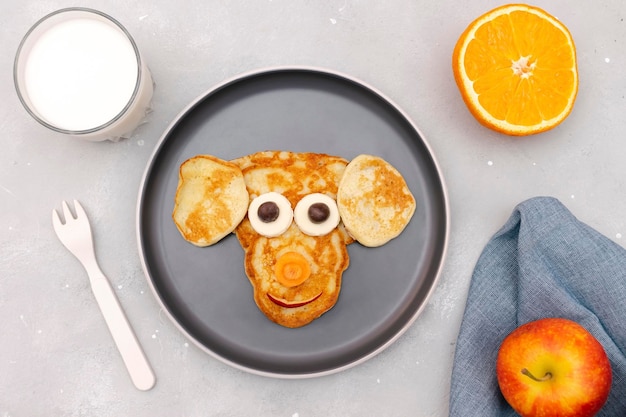 Funny monkeydog face shape snack from pancakecheese on plate Cute kids childrens baby's sweet dessert healthy breakfastlunch food art with milkapples on gray concrete backgroundtop view