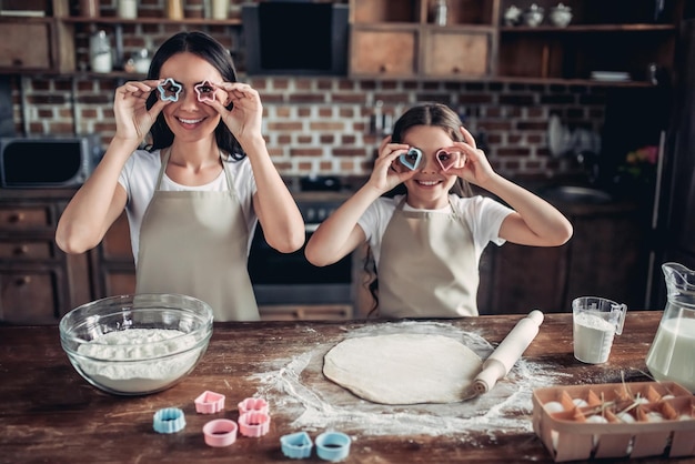 Funny mother and daughter covering eyes with cookie cutters on the kitchen