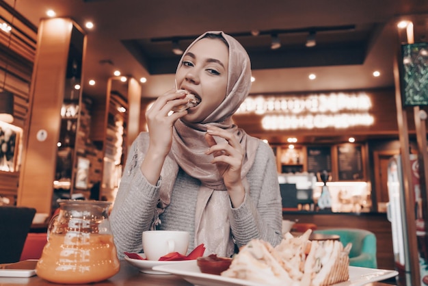 Funny Muslim girl in hijab at a cafe delicious food and tea