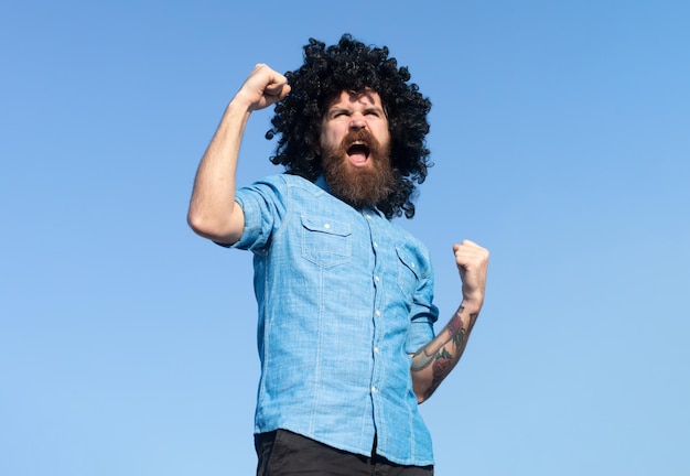 Funny nerdy guy crazy funny bearded man with wig on sky background expression and success