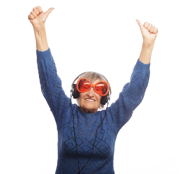 Funny old lady listening music and showing thumbs up. Isolated on white.