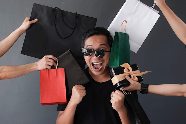 Photo funny online shopping sales with silly expression shopaholic man by many hands holding shoping bags