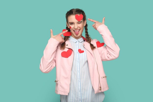 Photo funny optimistic teenager girl standing covered with little red hearts showing tongue out winking